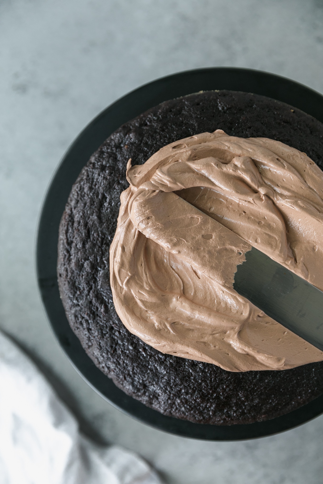 Overhead close up shot of chocolate buttercream being spread on a dark chocolate cake layer