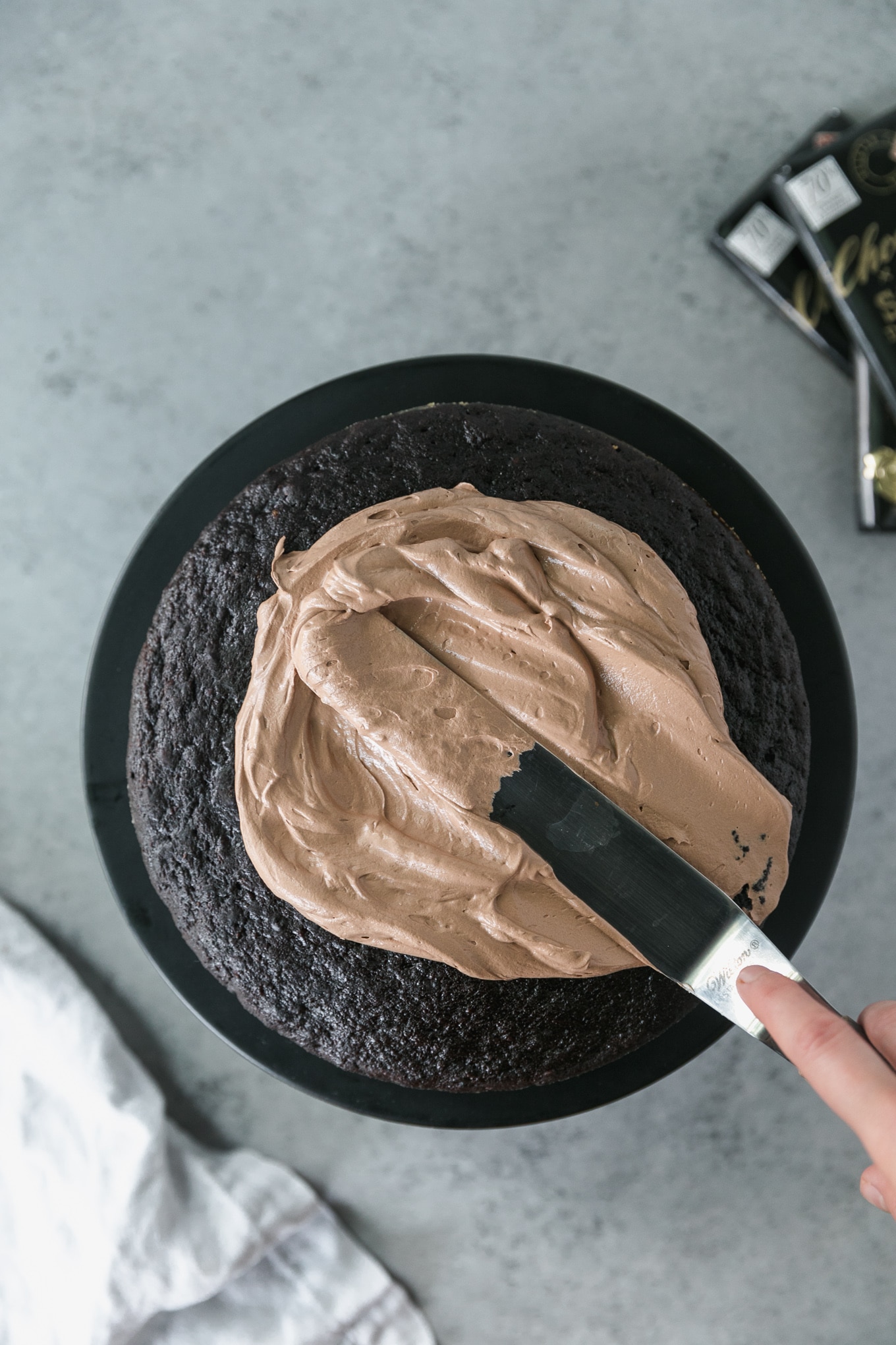 Overhead shot of chocolate buttercream being spread on a dark chocolate cake layer