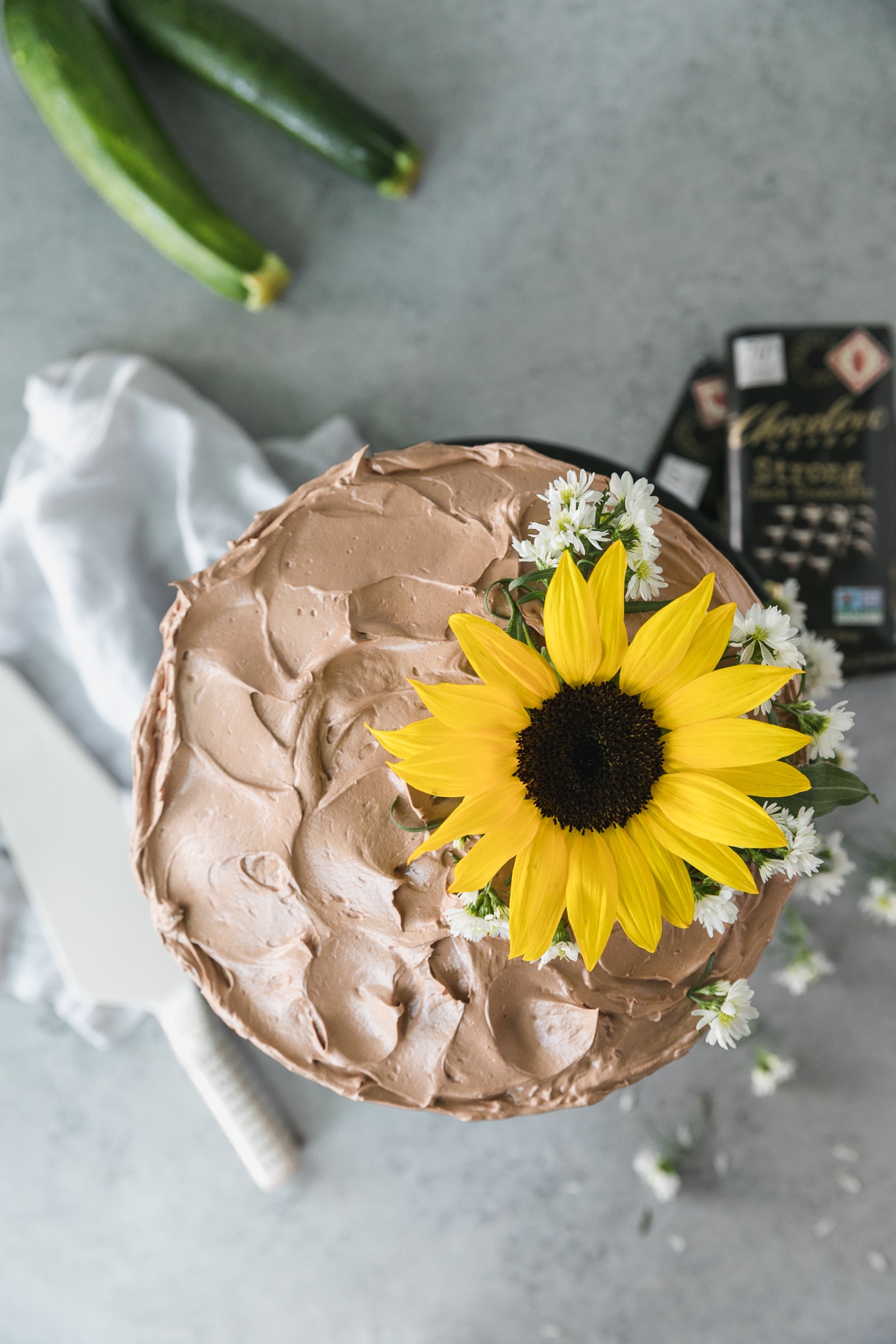 Overhead shot of a chocolate cake topped with a sunflower and small white flowers