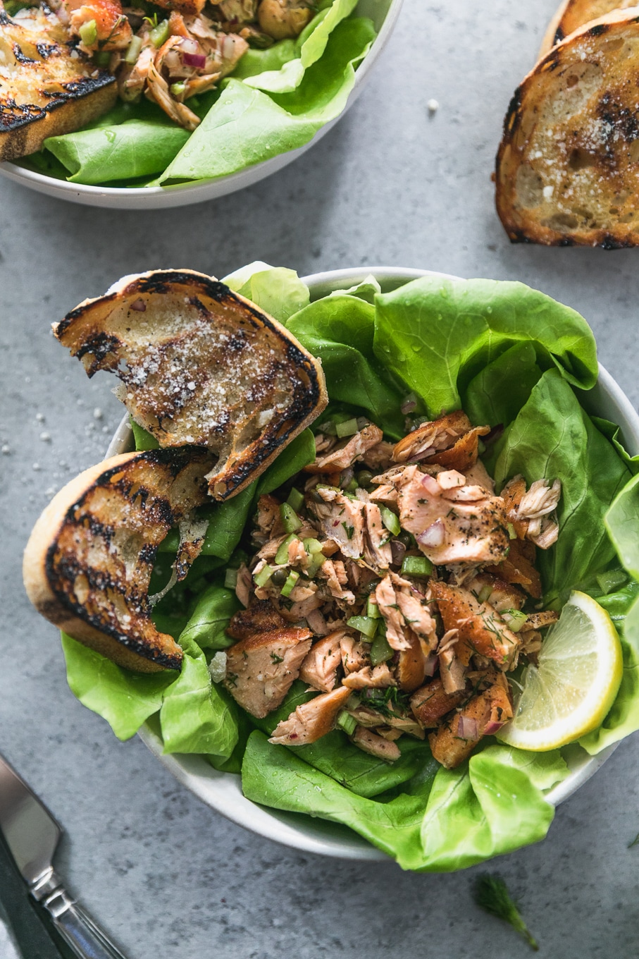 Overhead close up shot of a bowl of butter lettuce, flaked salmon, and grilled garlic bread