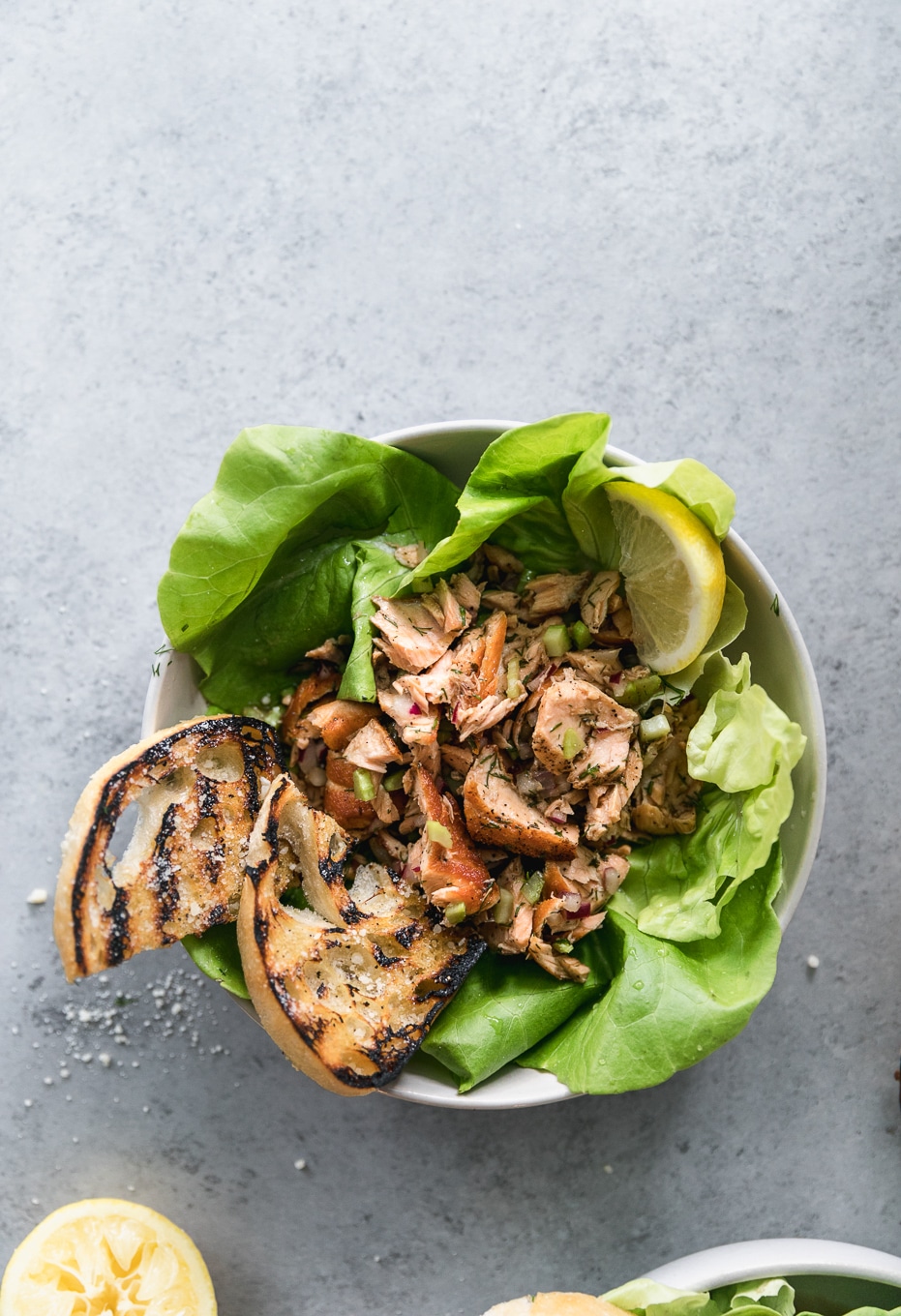 Overhead shot of a bowl of butter lettuce topped with flaked salmon, grilled garlic bread, and a lemon wedge