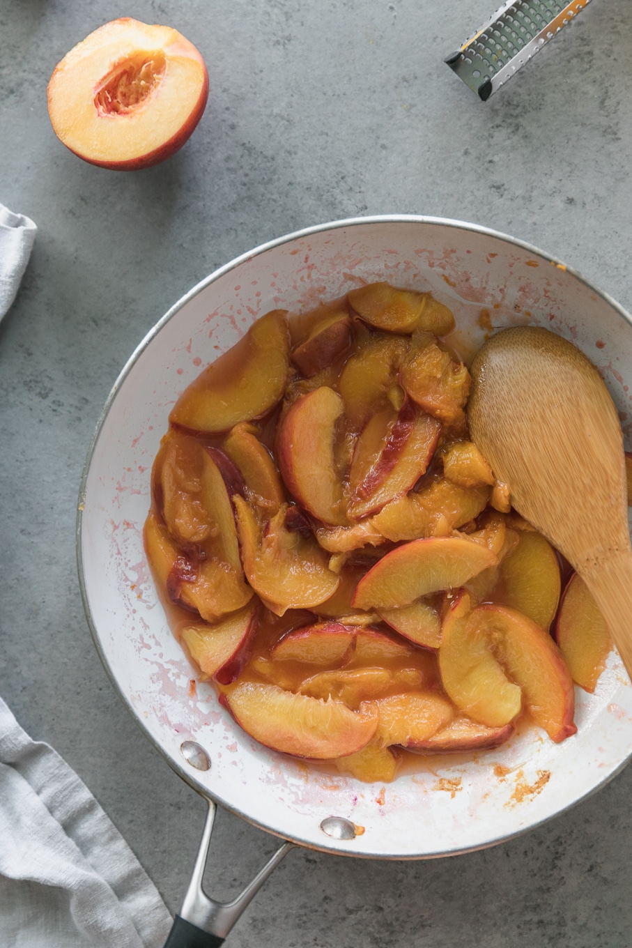 Overhead shot of a skillet filled with sautéed peaches with a wooden spoon in the skillet