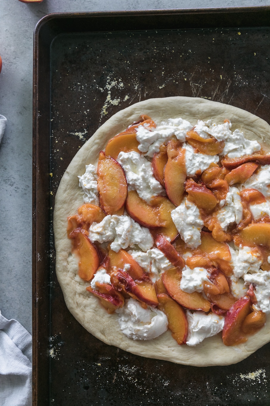 Overhead shot of rolled out pizza dough on a baking sheet topped with sliced peaches, chunks of burrata, and orange zest