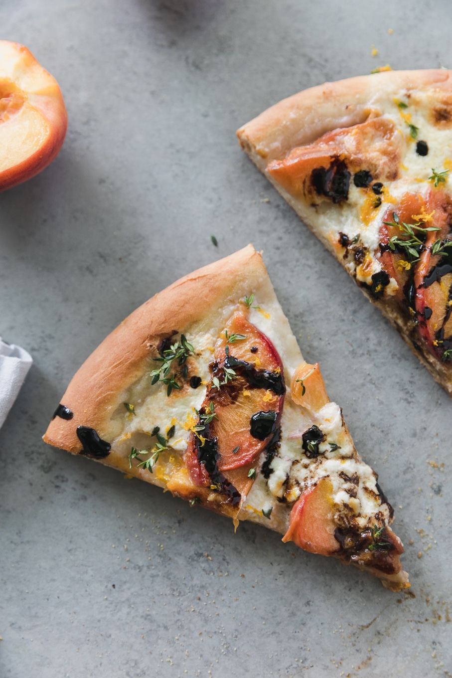 Overhead close up shot of a slice of pizza topped with peaches, thyme, balsamic glaze, and burrata