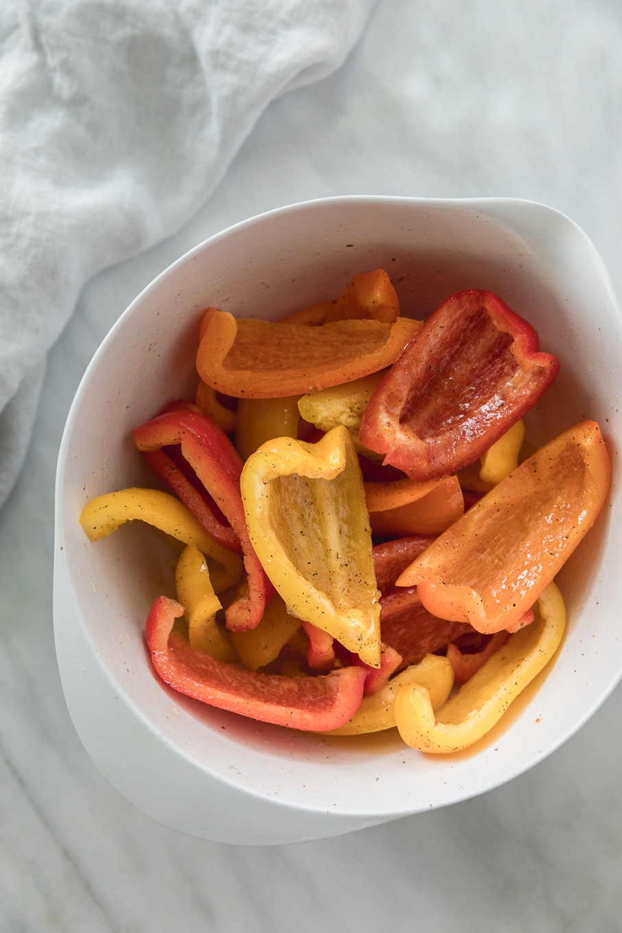 Overhead shot of a white bowl filled with three different colors of thickly sliced bell peppers