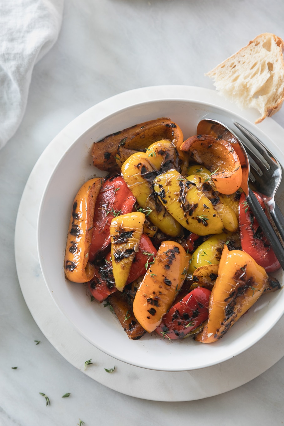 Overhead shot of a bowl of grilled peppers with a large spoon and fork in the bowl