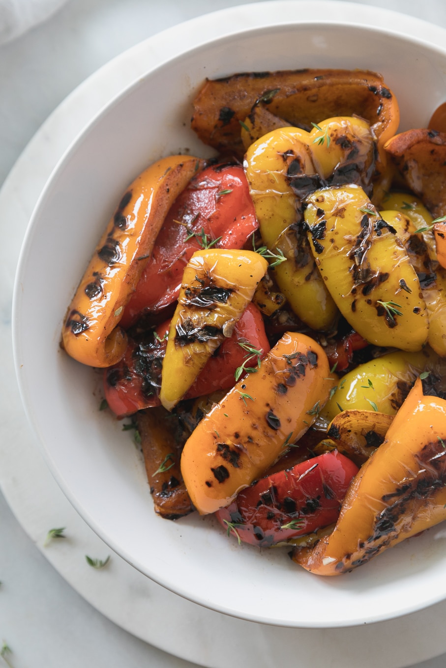 Overhead close up shot of a bowl of grilled peppers sprinkled with fresh thyme