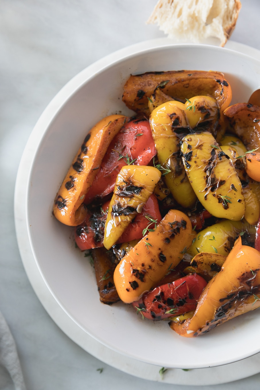 Overhead close up shot of a bowl of grilled peppers sprinkled with fresh thyme