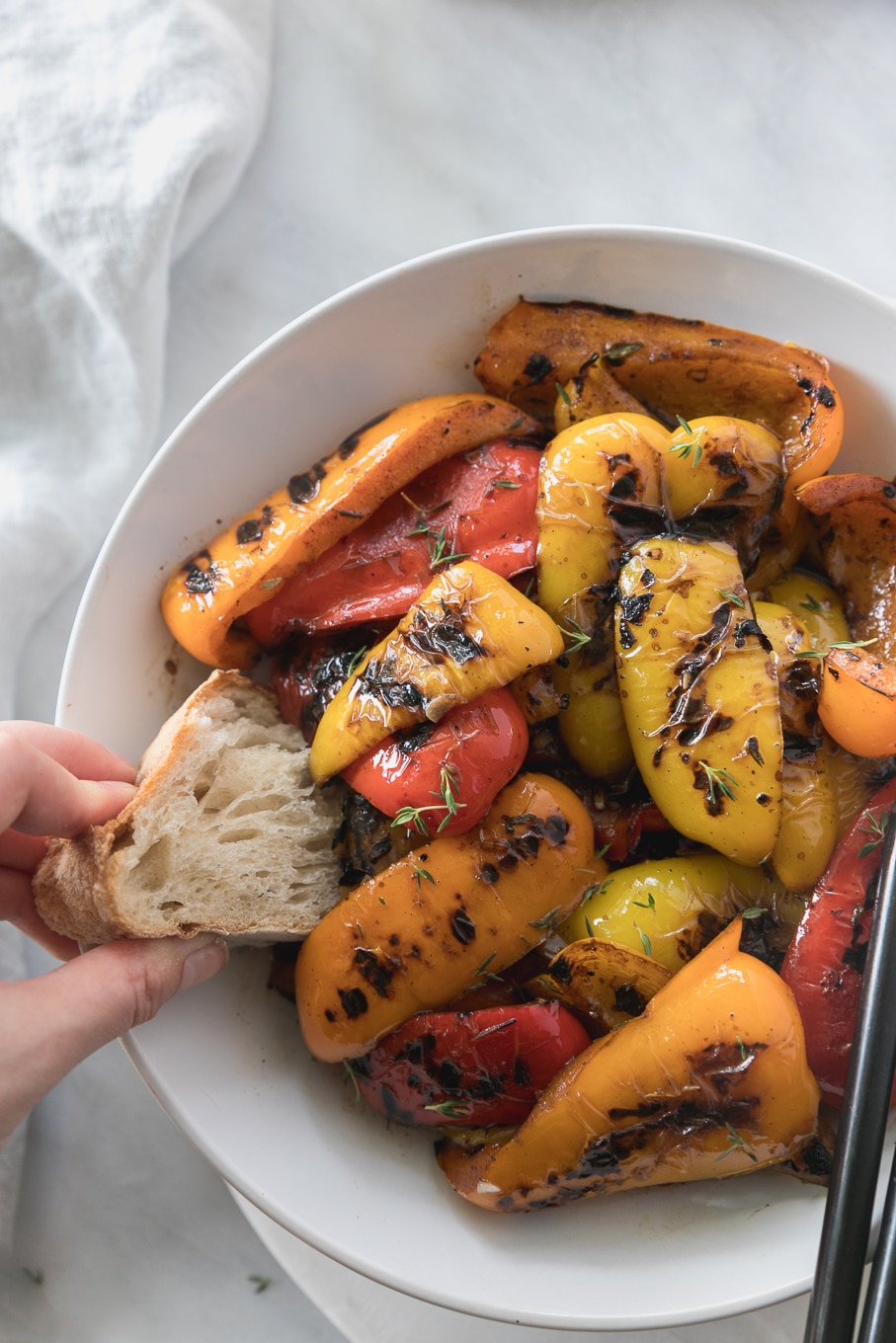 Overhead close up shot of a bowl of grilled peppers with a hand dipping a piece of bread into it