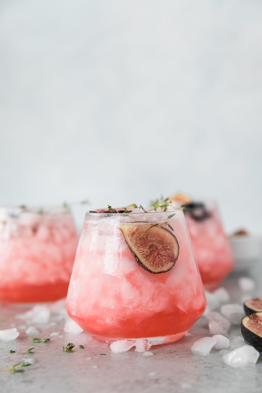 Forward facing shot of 3 bright pink fig thyme shrub cocktails garnished with halved figs and sprigs of thyme