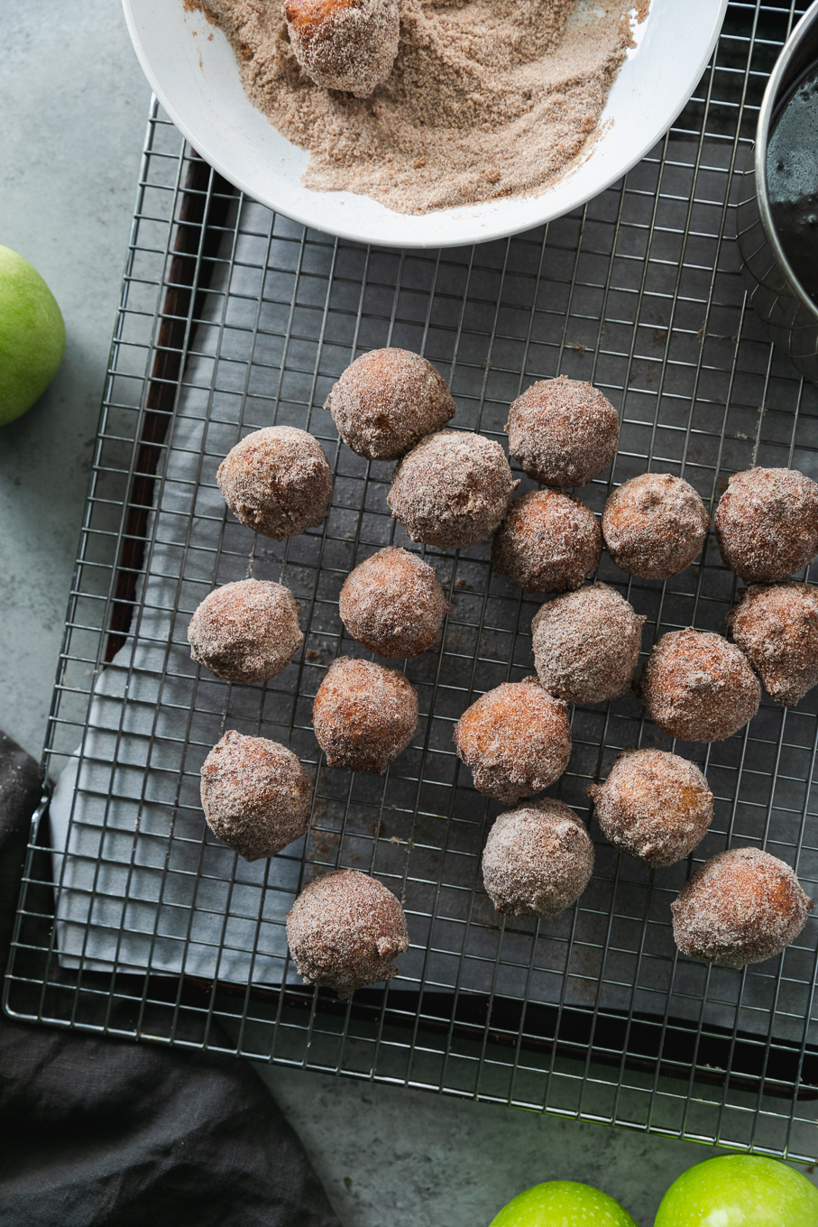 Overhead shot of a cooling rack with doughnut holes on top and a green apple next to it