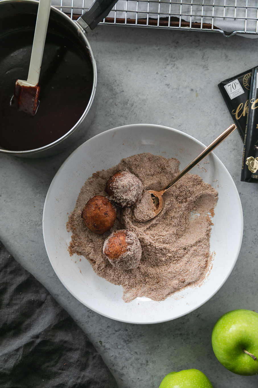 Overhead shot of a white shallow bowl filled with cinnamon sugar, doughnut holes, and a gold spoon
