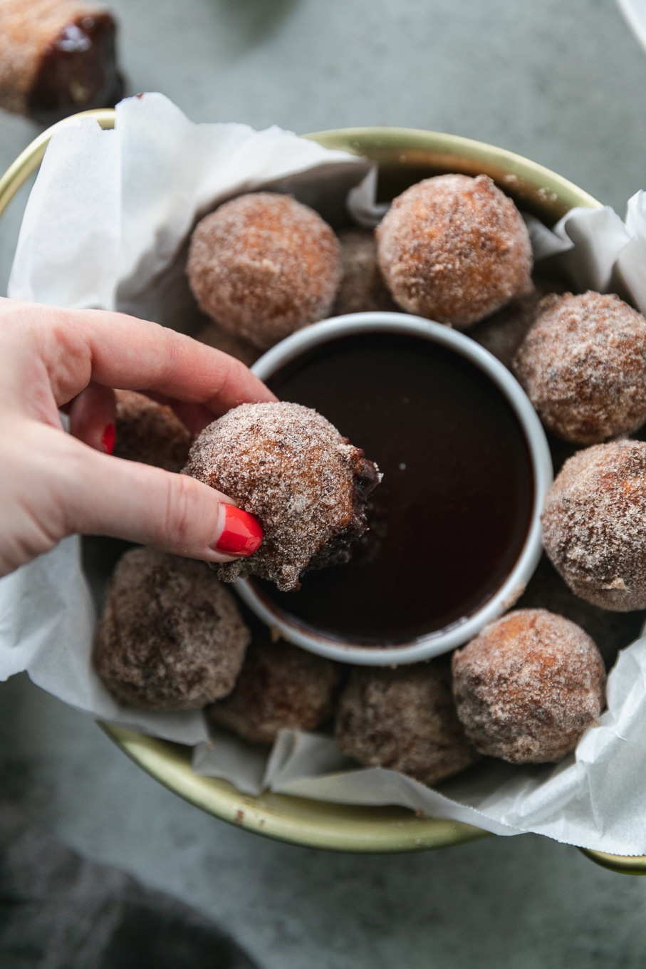 Overhead close up shot of a had dipping a doughnut hole into dark chocolate fudge sauce