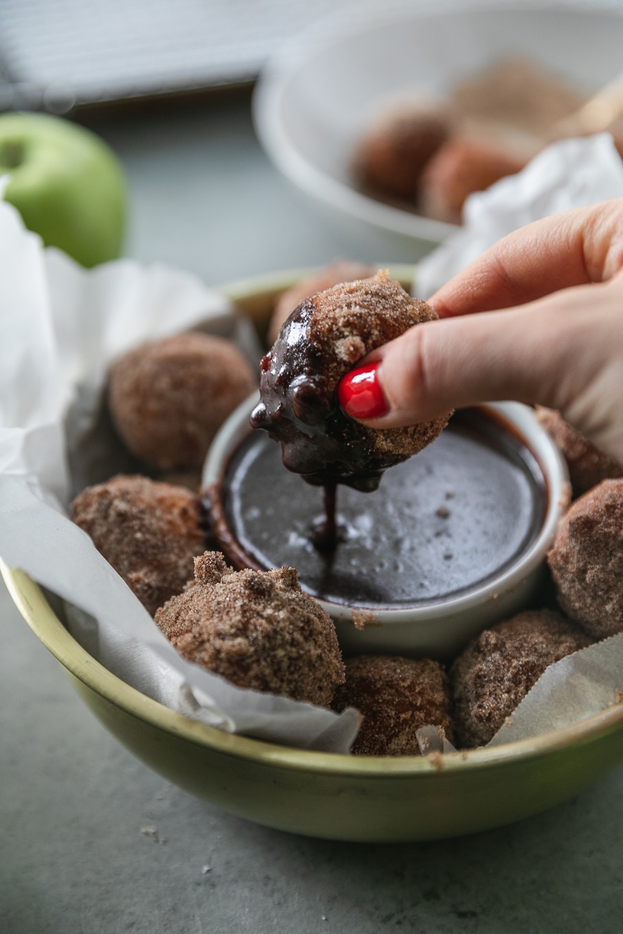 Close up shot of a had dipping a doughnut hole into dark chocolate fudge sauce