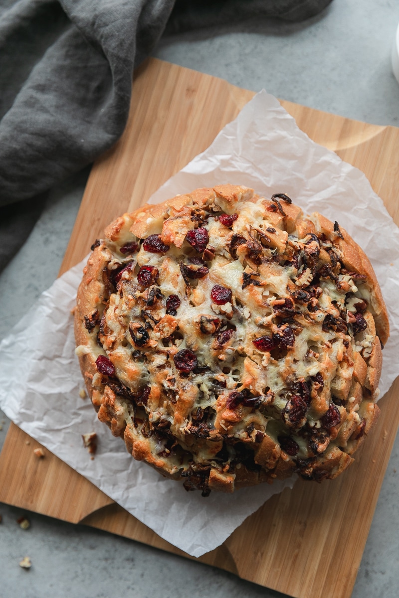 Overhead shot of a circular loaf of bread stuffed with melted cheese, caramelized onions, cranberries, and pecans
