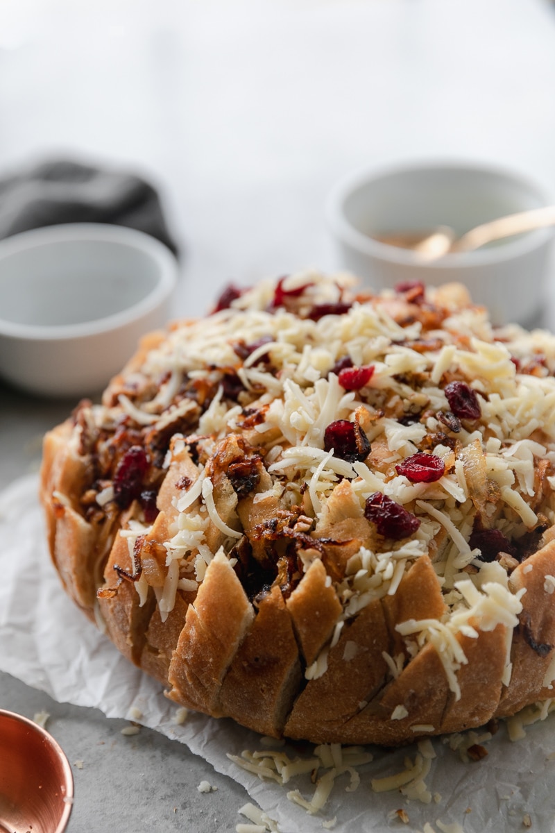 Close up shot of a loaf of bread stuffed with shredded cheese, caramelized onions, cranberries, and pecans