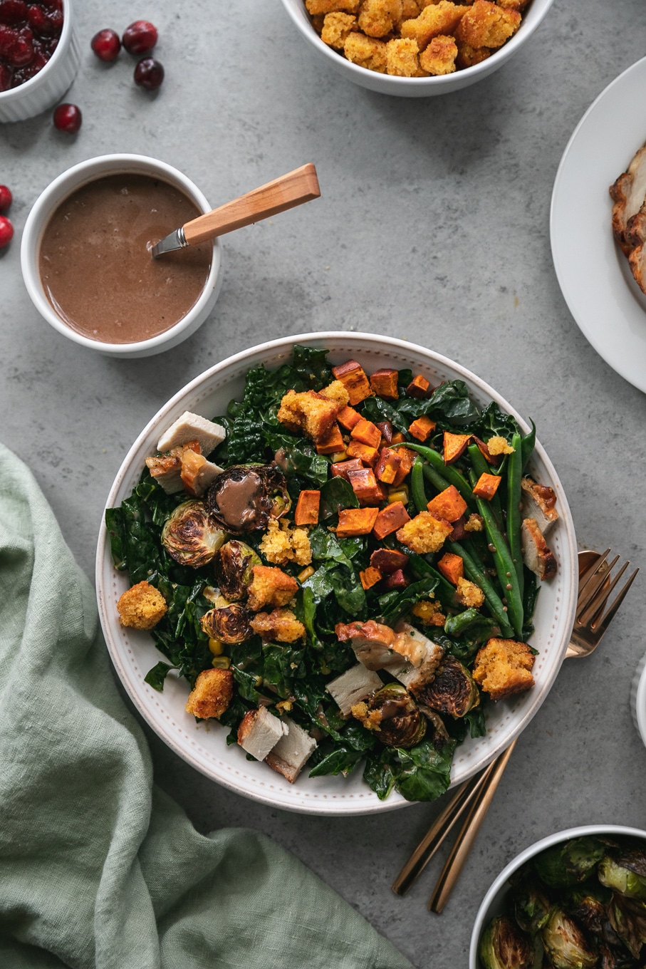Overhead shot of a thanksgiving leftovers kale salad with roasted sweet potatoes, brussels, green beans, and cornbread croutons with a ramekin of cranberry balsamic vinaigrette above it