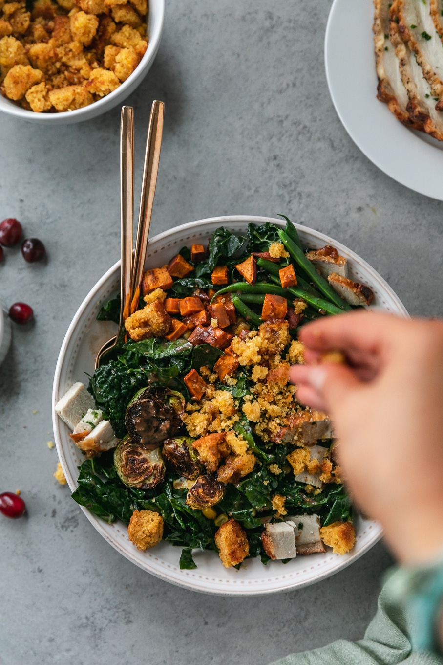 Overhead shot of a thanksgiving leftovers kale salad being sprinkled with cornbread croutons