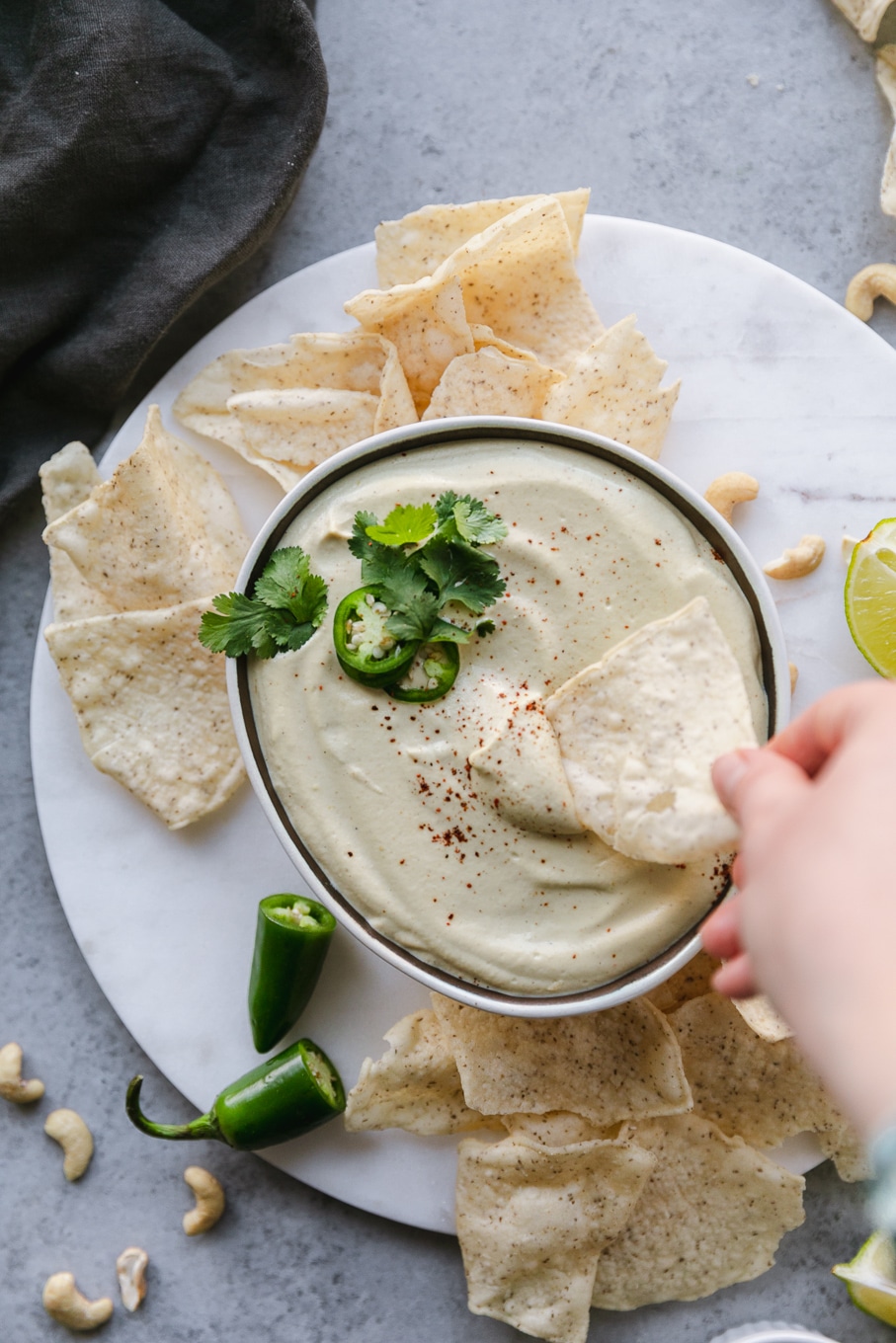 Overhead close up shot of a bowl of cashew queso and a chip resting on top half dipped in queso