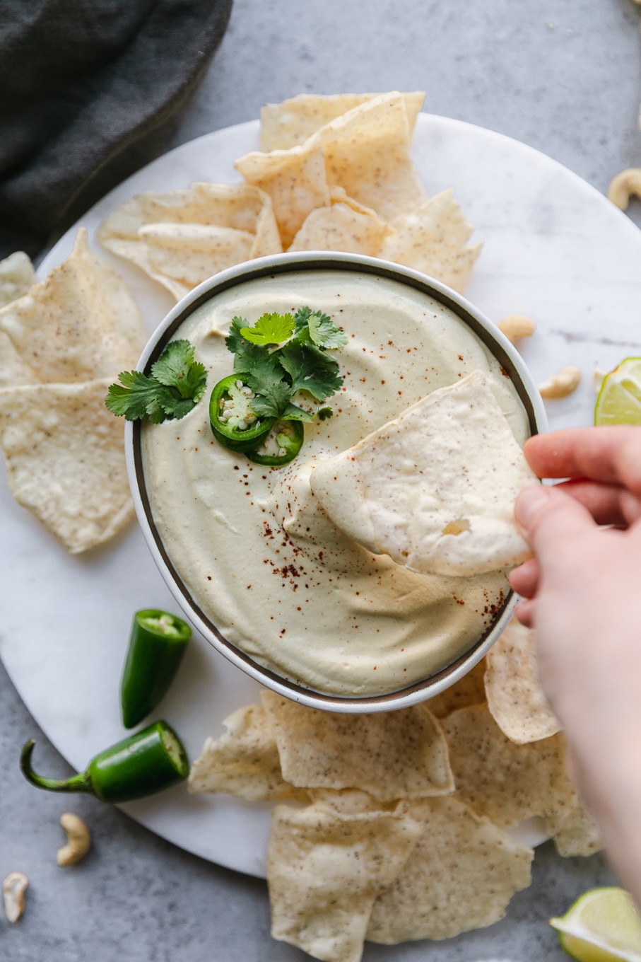Overhead shot of a bowl of queso and a hand dipping a chip in it and chips scattered around the bowl
