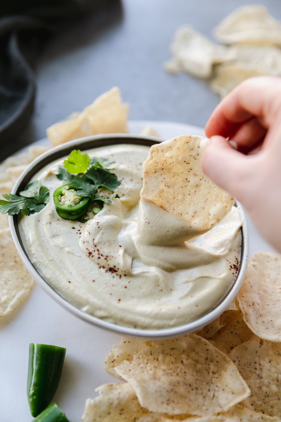 Close up shot of a bowl of queso and a hand dipping a chip in it and chips scattered around the bowl