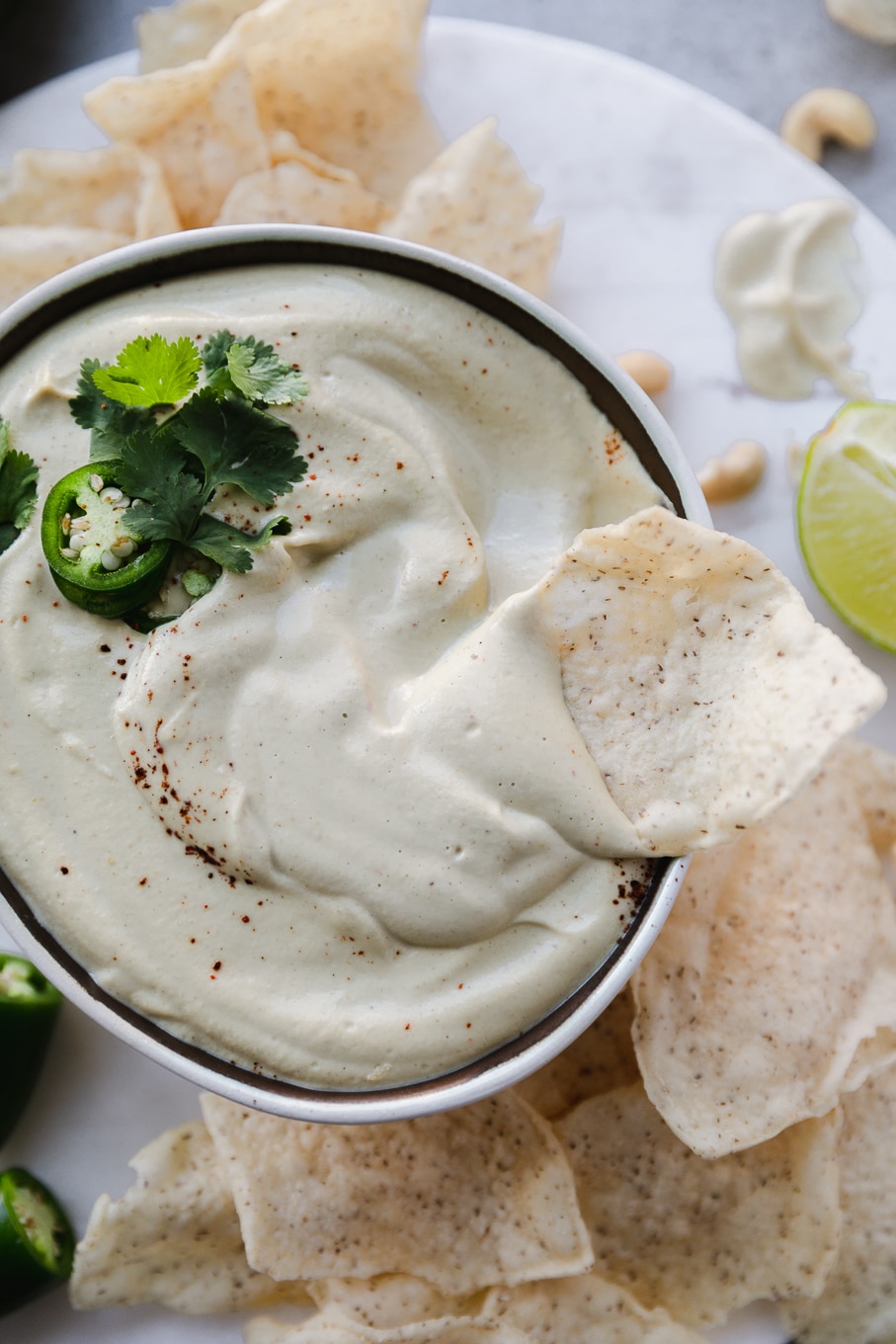 Overhead close up shot of a bowl of cashew queso with a chip resting on top half dipped in queso