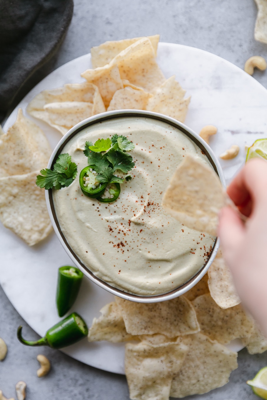 Close up shot of a bowl of queso and a hand dipping a chip in it