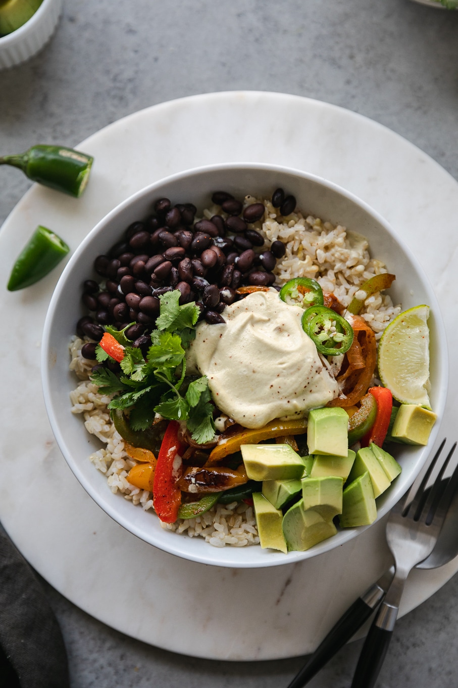 Overhead close up shot of a burrito bowl filled with brown rice, black beans, fajita veggies, avocado, lime, cilantro and cashew queso