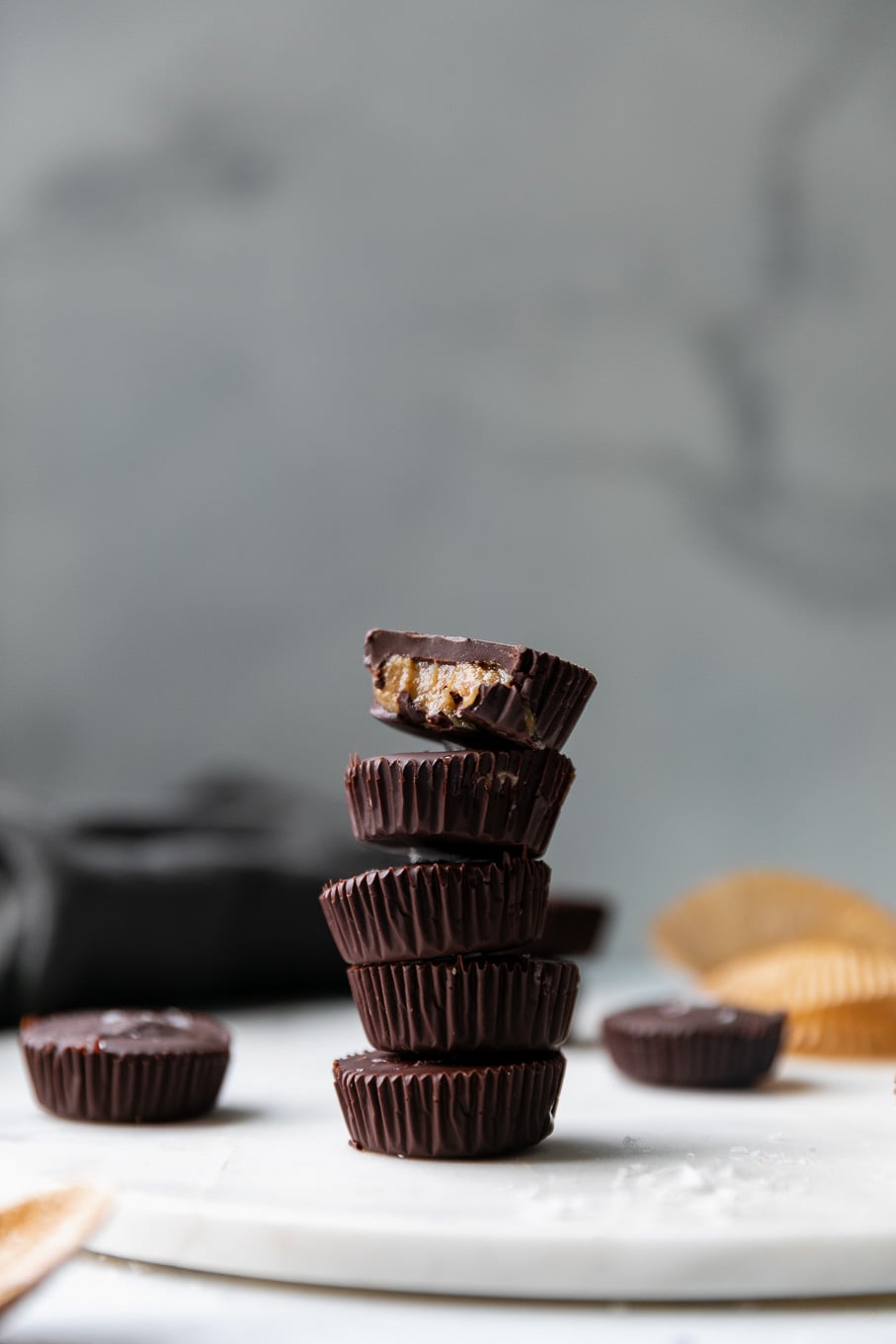 Forward facing shot of a stack of dark chocolate tahini cups with a bite taken out of the one on top