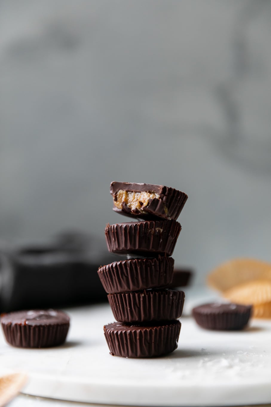 Forward facing shot of a stack of dark chocolate tahini cups with a bite taken out of the one on top