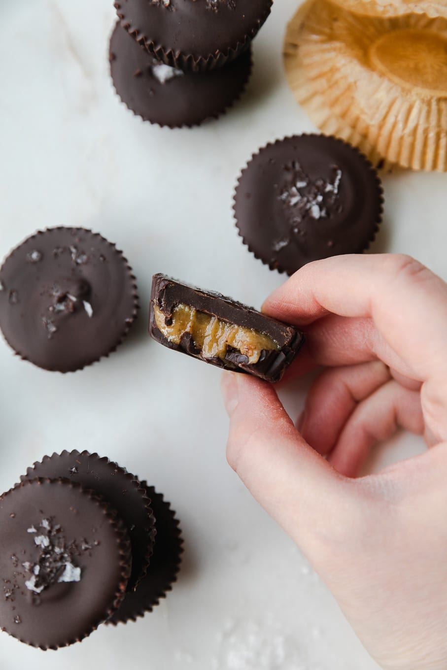 Overhead shot of a hand holding a dark chocolate tahini cup with a bite taken out of it