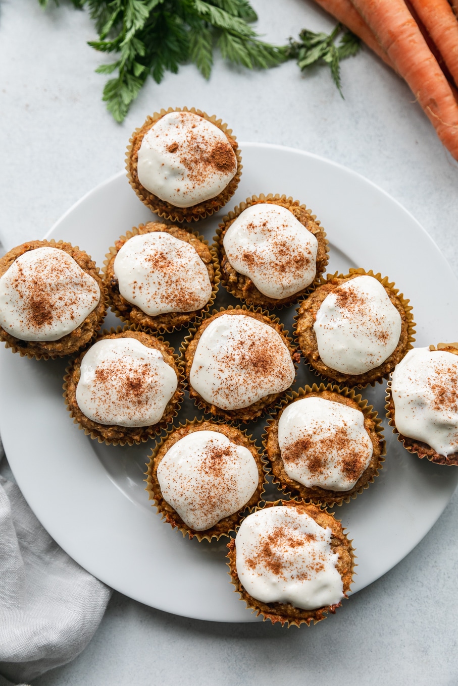 Overhead shot of a white plate with cream cheese glared carrot cake muffins on top