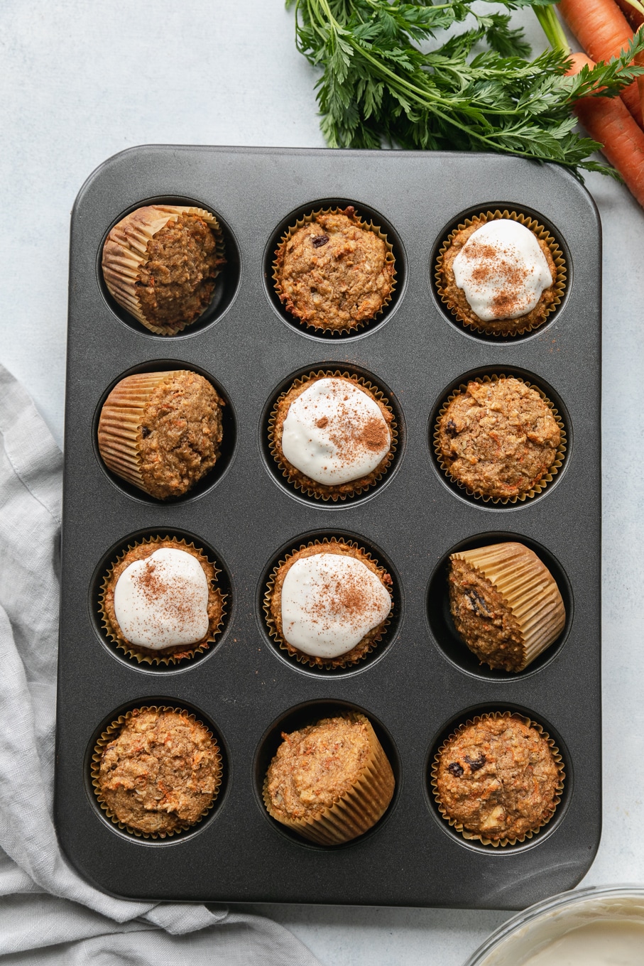 Overhead shot of carrot cake muffins in a muffin tin with cream cheese glaze on some of them