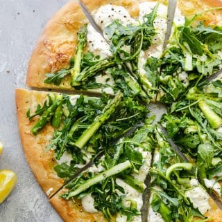 Overhead shot of a pizza cut into triangles topped with a shaved asparagus arugula salad