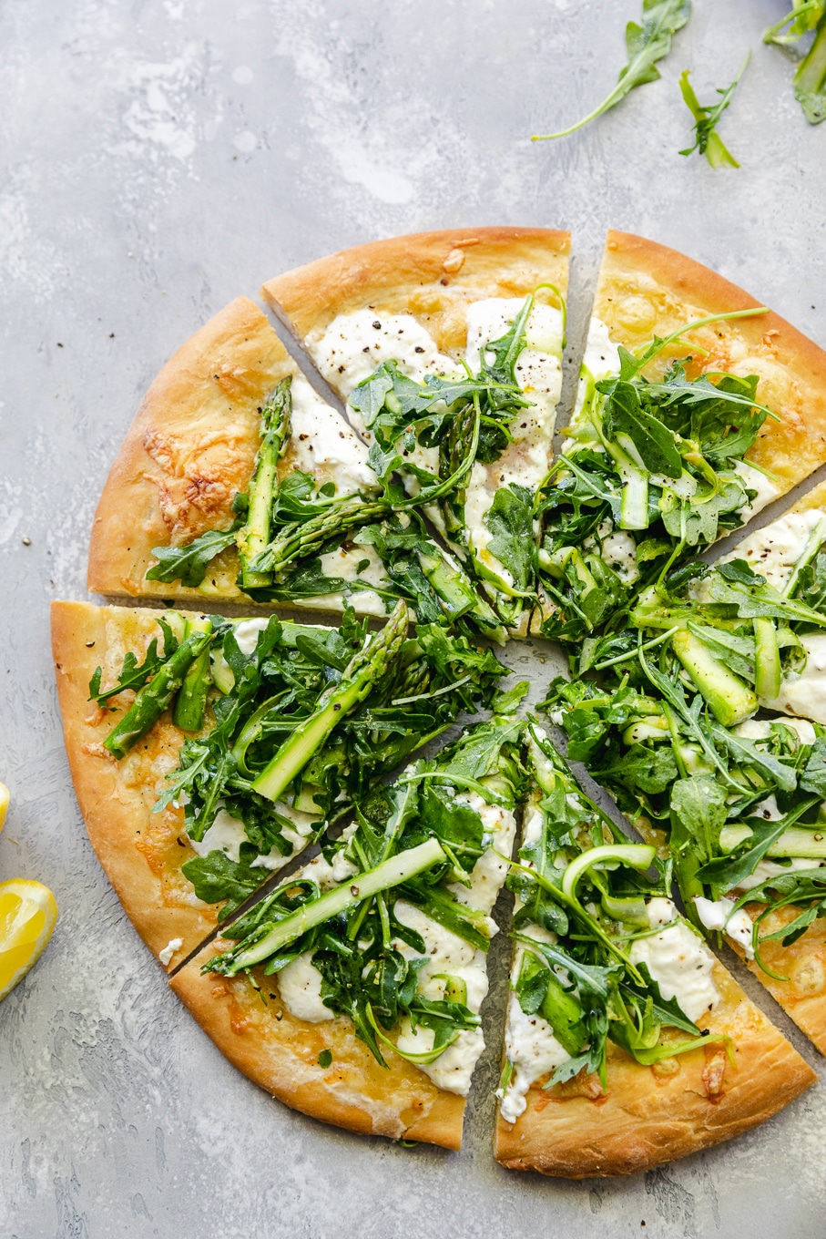 Overhead shot of a pizza cut into triangles topped with a shaved asparagus arugula salad