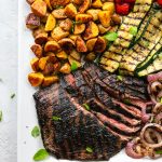 Overhead shot of a platter of flank steak, grilled vegetables, and roasted potatoes