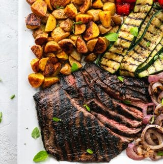 Overhead shot of a platter of flank steak, grilled vegetables, and roasted potatoes
