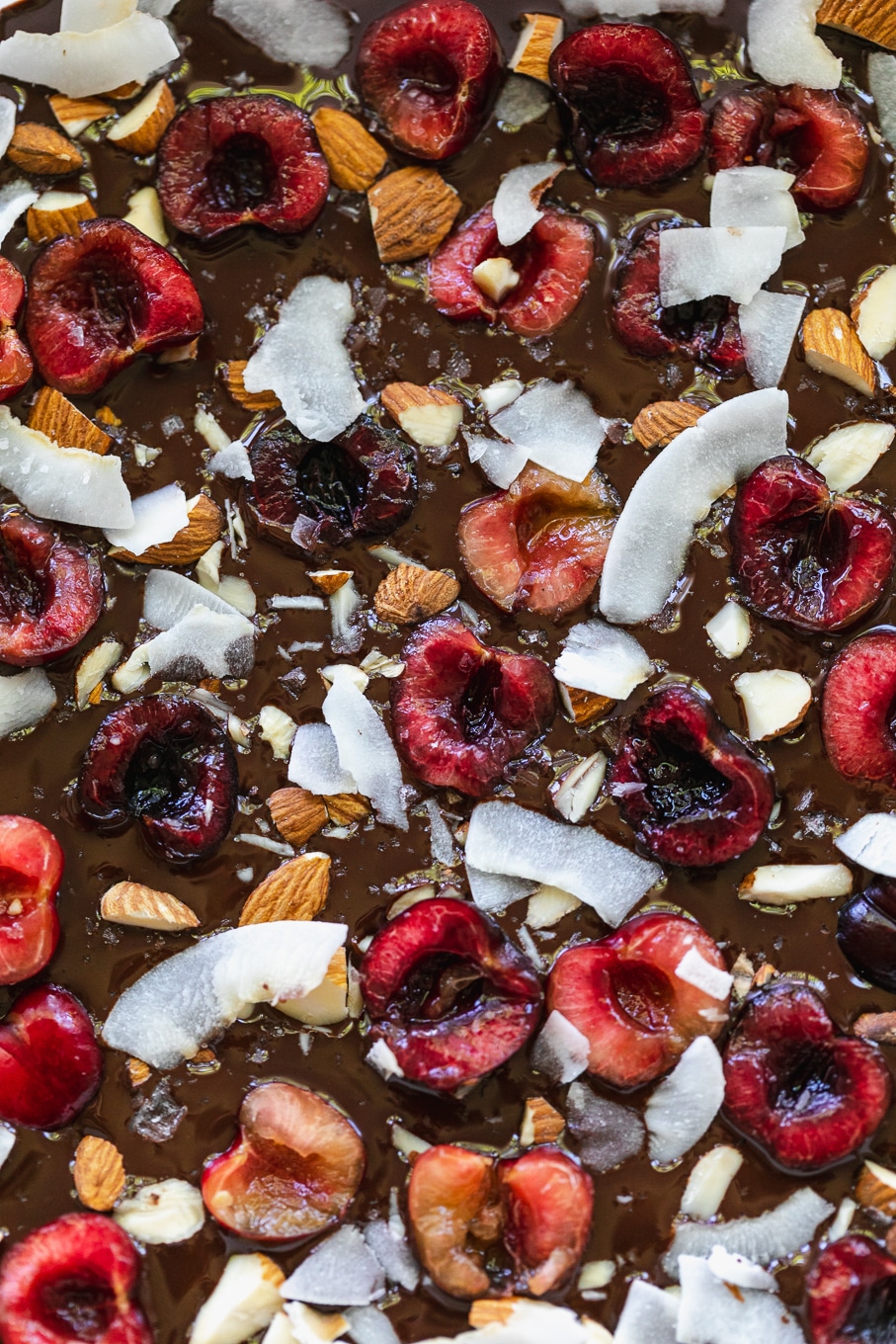 Overhead close up shot of bars with melted chocolate, halved cherries, almonds, and coconut