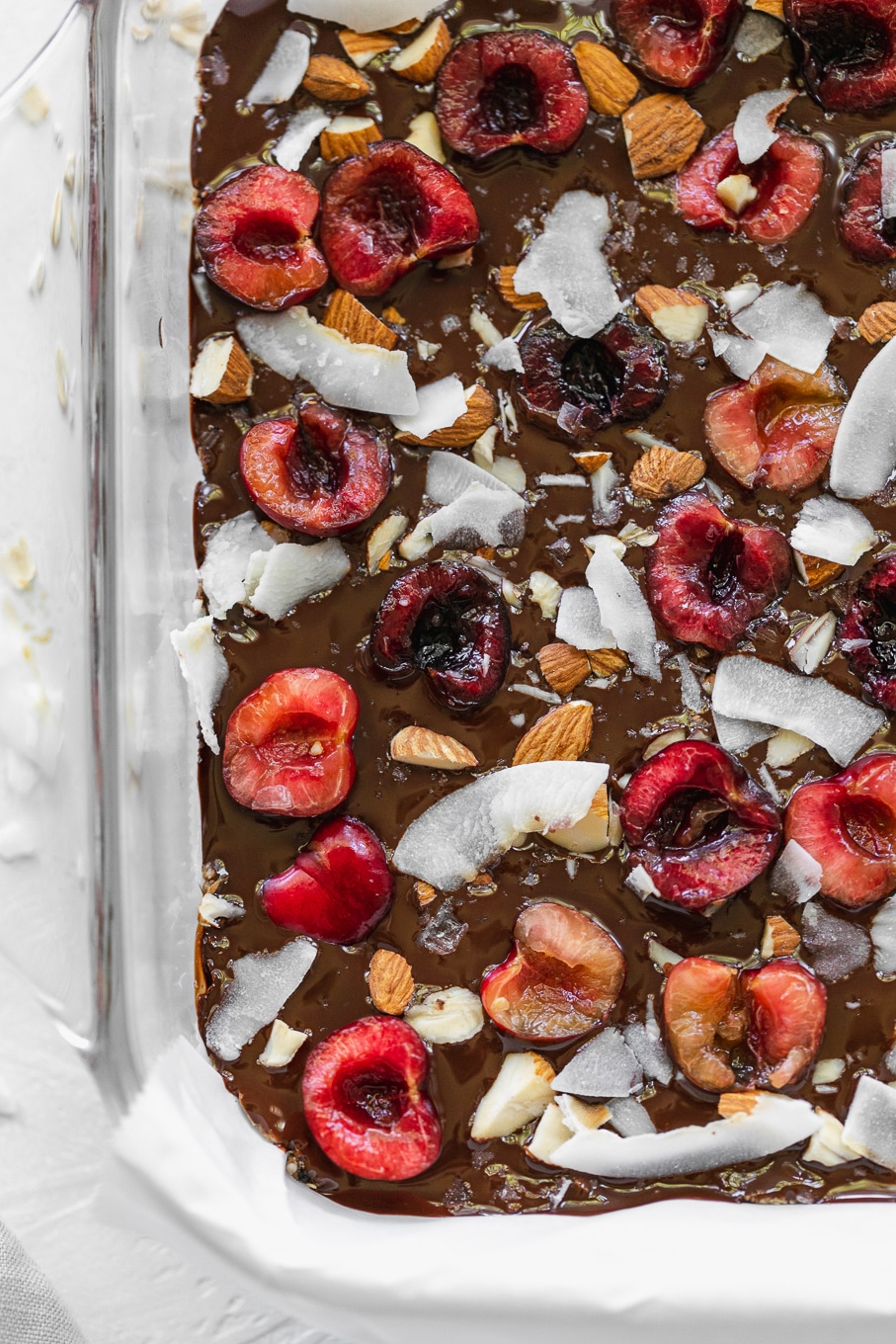 Overhead shot of a pan of bars with melted chocolate, halved cherries, almonds, and coconut