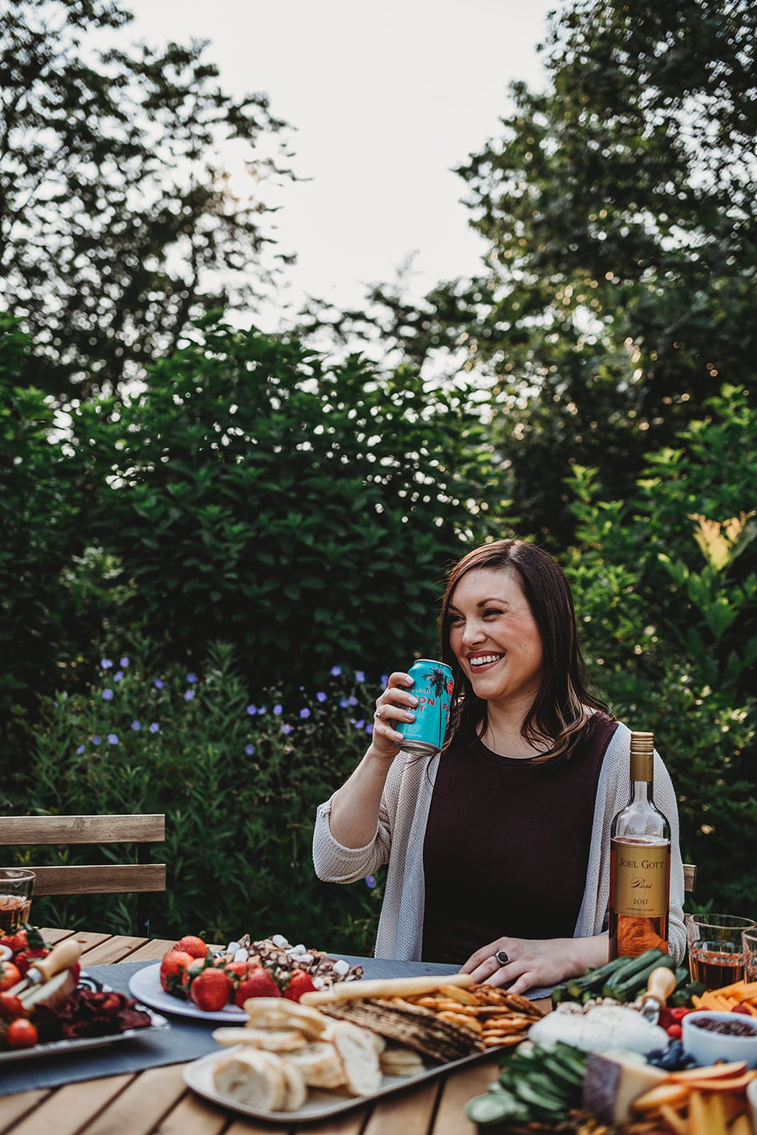 Shot of a smiling woman sitting at a beautiful tables cape in a garden holding a can of beer