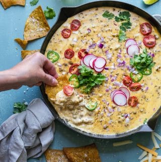 Overhead shot of a hand dipping a chip into a skillet of taco beer cheese dip