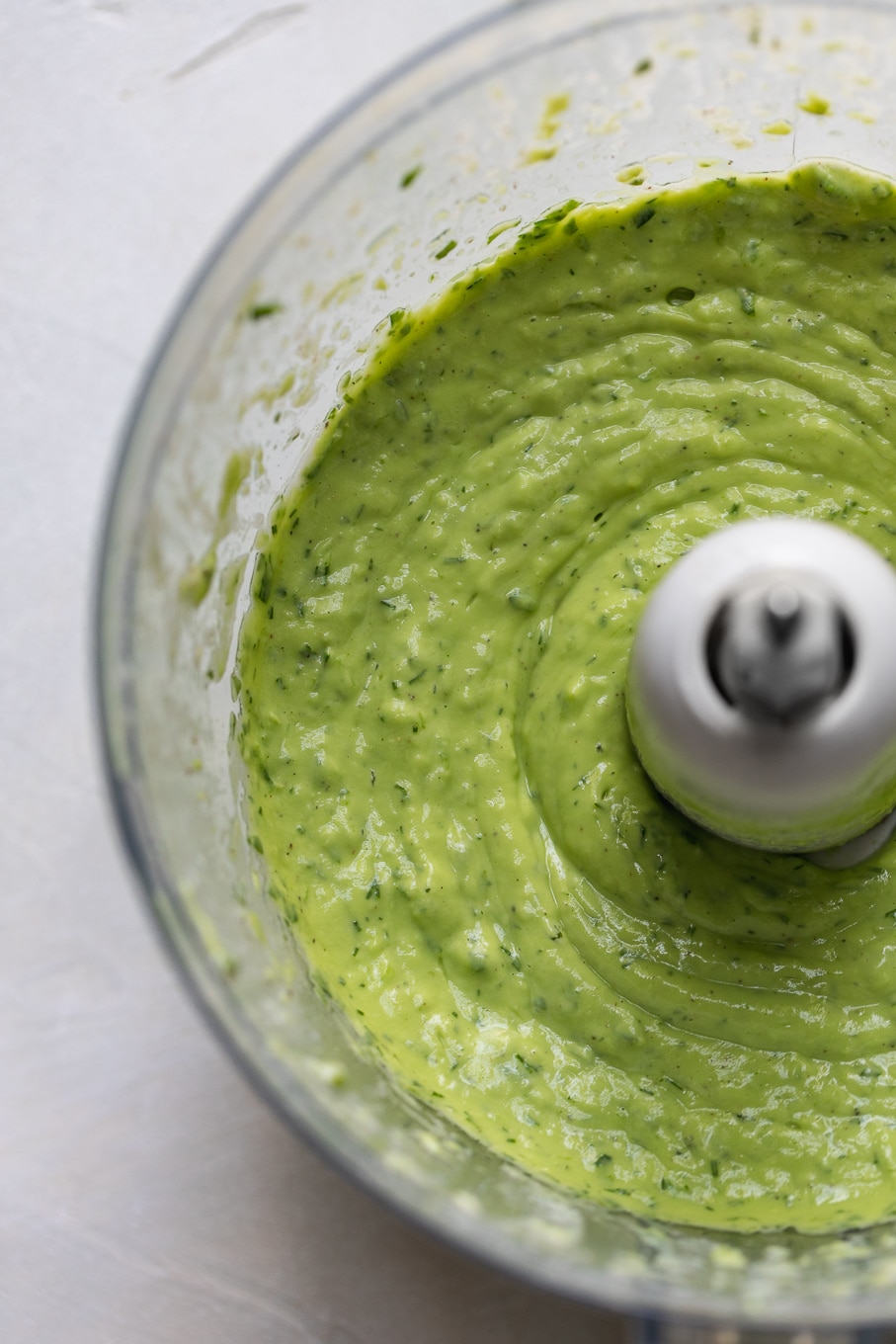 Overhead close up shot of a food processor filled with creamy green avocado ranch