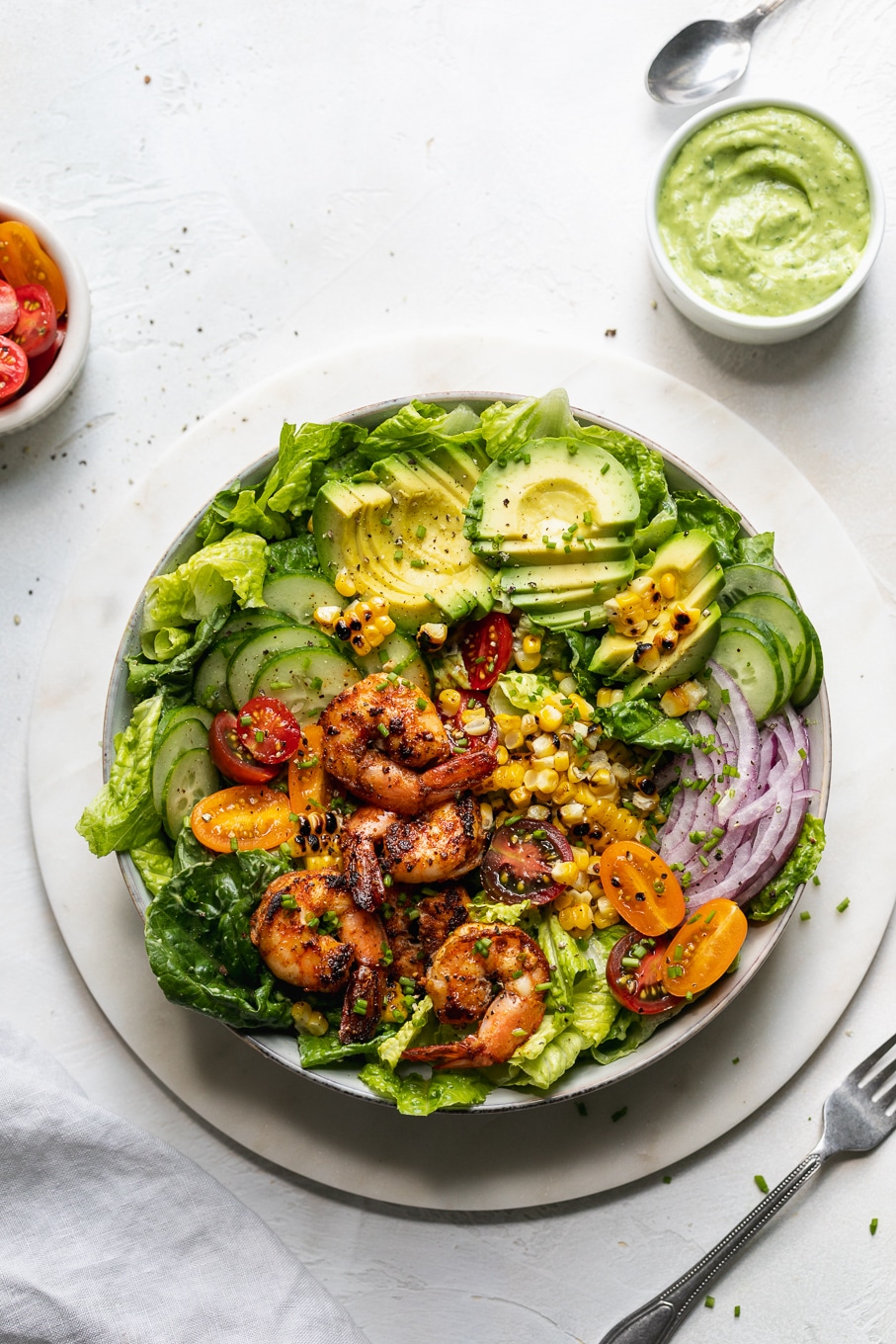 Overhead shot of a colorful blackened shrimp salad with grilled corn, avocado, red onion, tomatoes, and cucumber