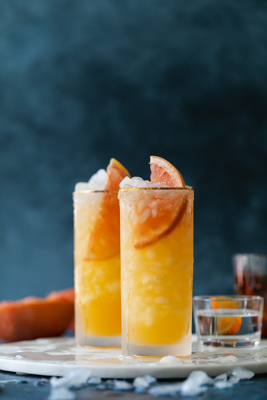 Straight on shot of grapefruit cocktails against a dark blue background