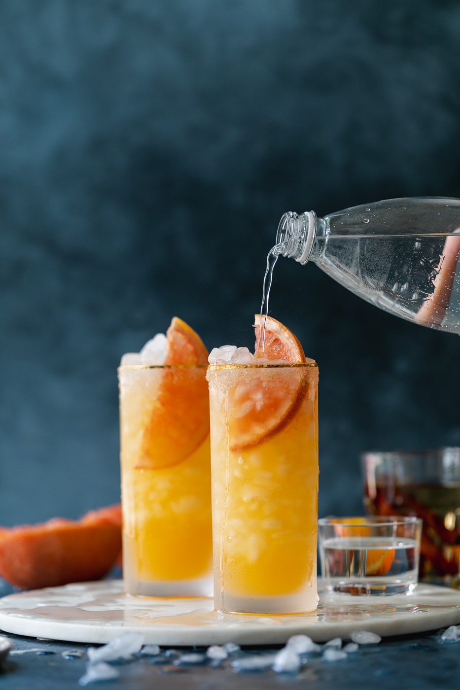 Straight on shot of soda water pouring into a cocktail against a dark blue background