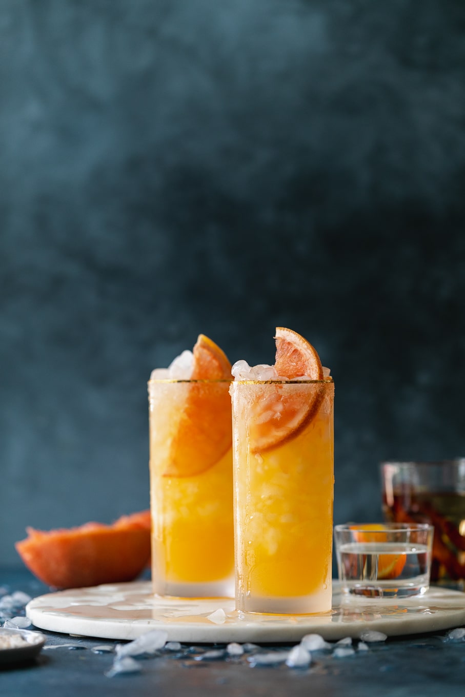 Straight on shot of grapefruit cocktails against a dark blue background