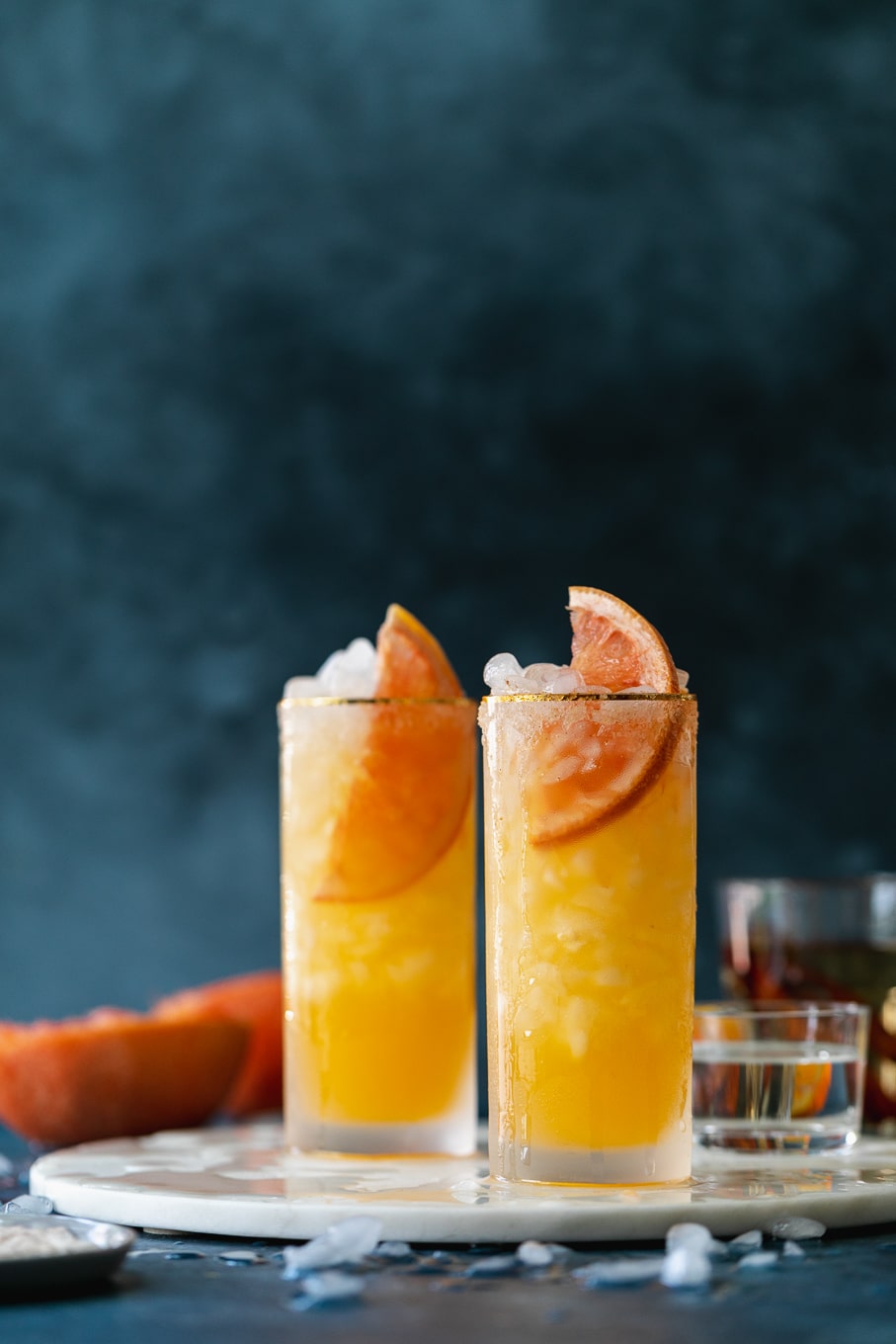 Straight on shot of grapefruit cocktails against a dark blue background