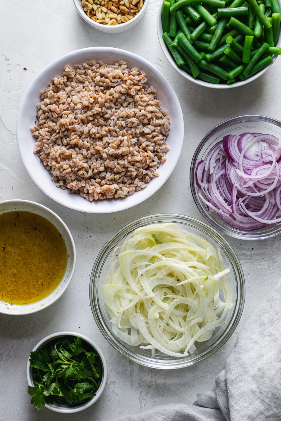 Overhead shot of bowls filled with pine nuts, red onion, green beans, and fennel