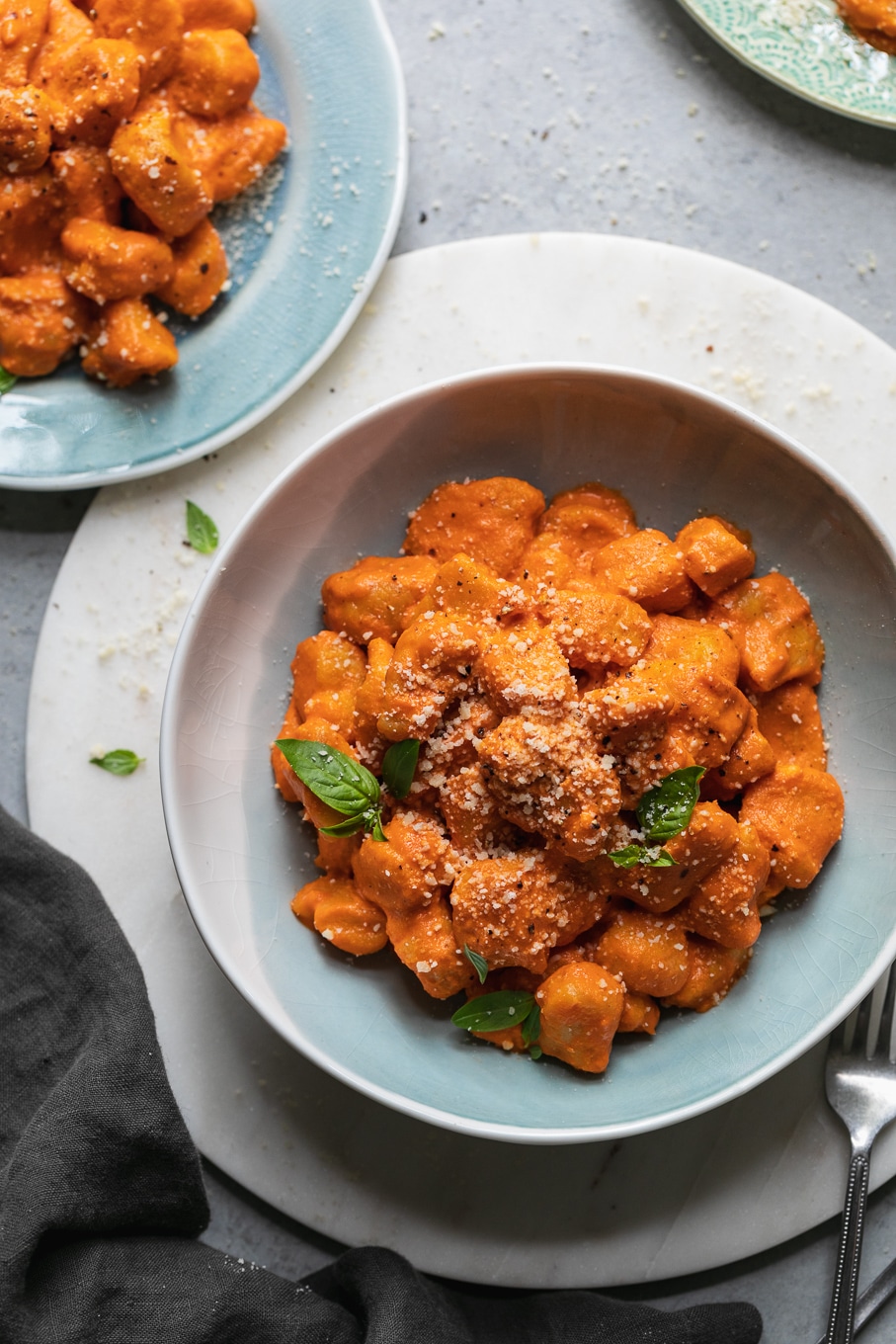 Overhead shot of a bowl and a plate of gnocchi with vodka sauce and basil