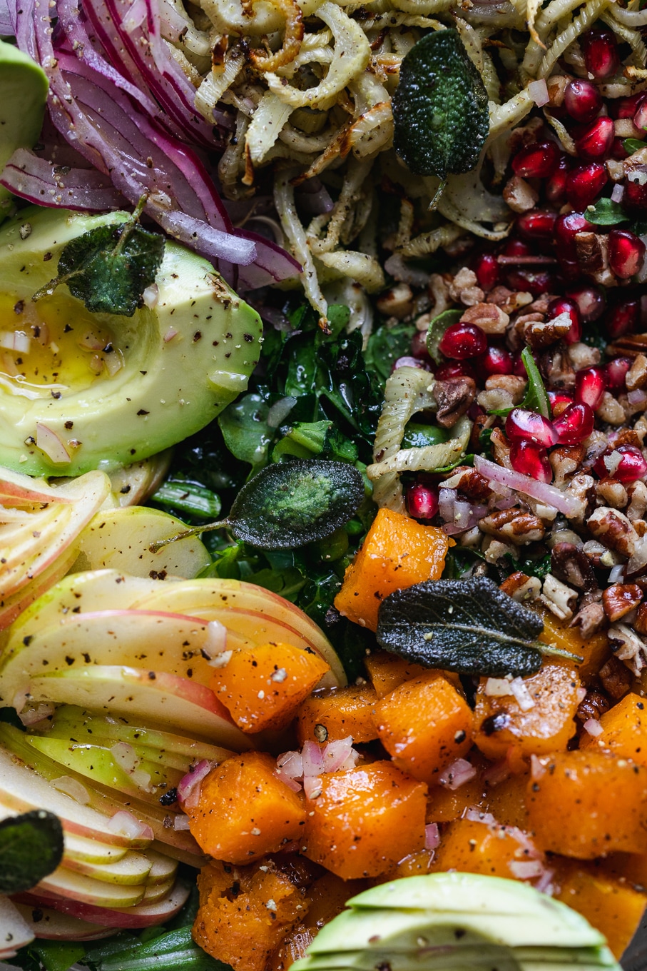 Very close up shot of avocado, apple, butternut squash, pecans, pomegranate, red onion, and fried sage
